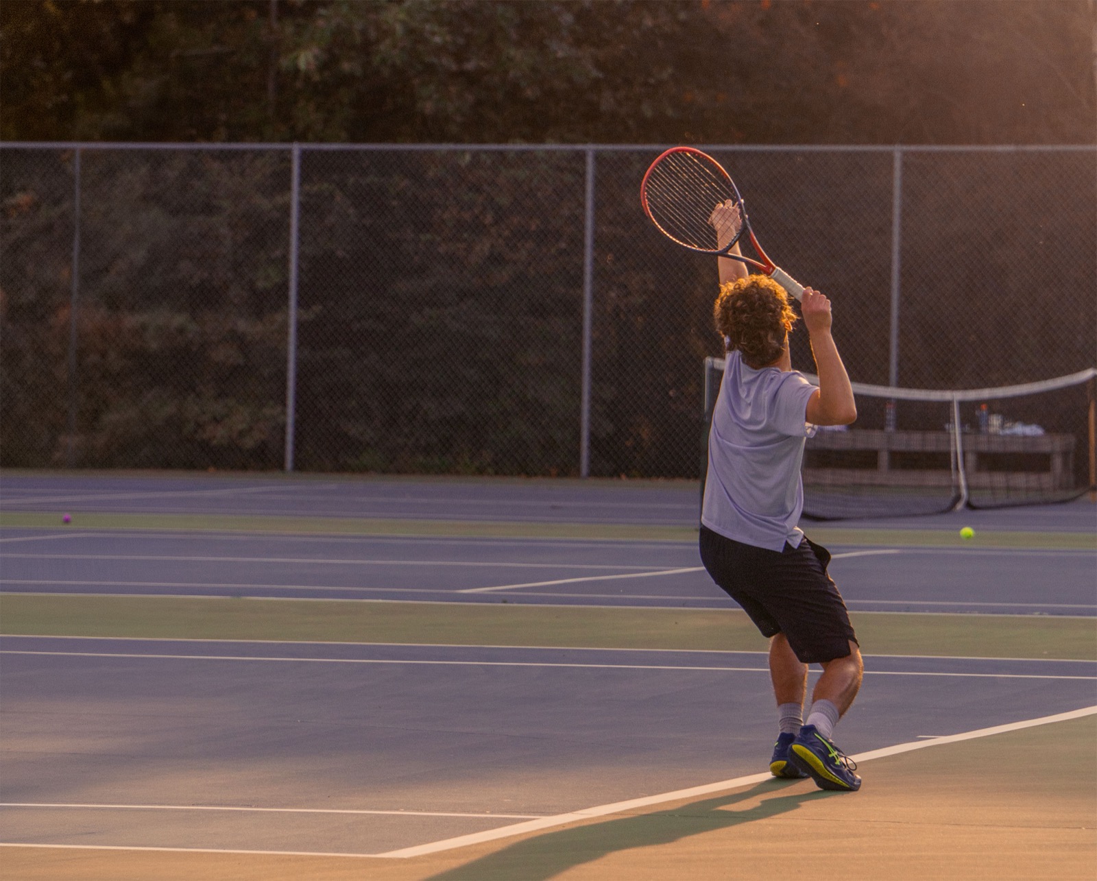 Tennis player mid-serve on a PEI court at golden hour